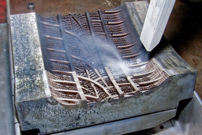 Primer plano de un proceso de limpieza en un molde de neumático caliente, eliminando residuos de caucho para reducir el tiempo de inactividad de la producción.