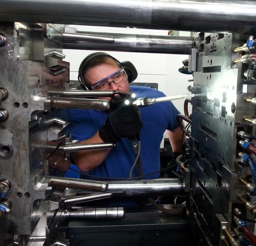 Operario con gafas y protectores auditivos realizando una limpieza de precisión en un molde de inyección para la industria del plástico con un método no abrasivo.